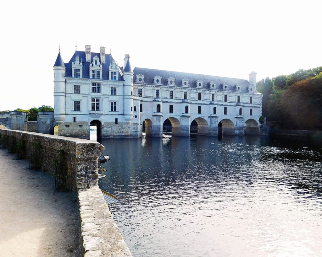 White Renaissance château with slate turrets and stone arches reflected in a calm river in France’s Loire Valley